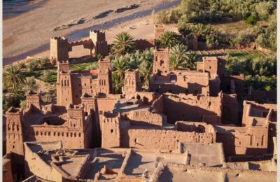 Scenic view of Kasbah Ait Ben Haddou, a UNESCO World Heritage site, surrounded by the arid Moroccan landscape under a clear blue sky.