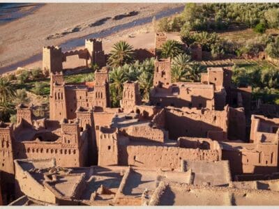 Scenic view of Kasbah Ait Ben Haddou, a UNESCO World Heritage site, surrounded by the arid Moroccan landscape under a clear blue sky.