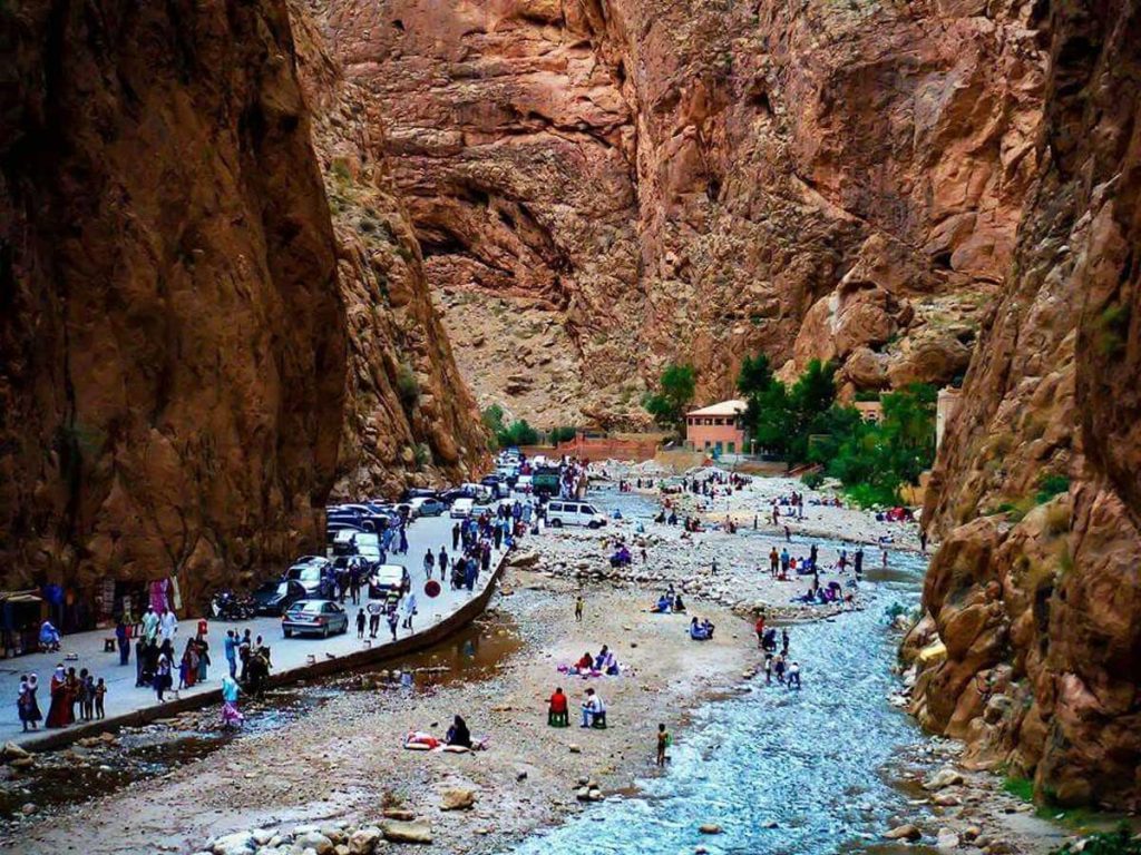 cenic view of Todra Gorge in Morocco, with steep canyon walls rising high on either side of a narrow stream that winds through the rocky landscape