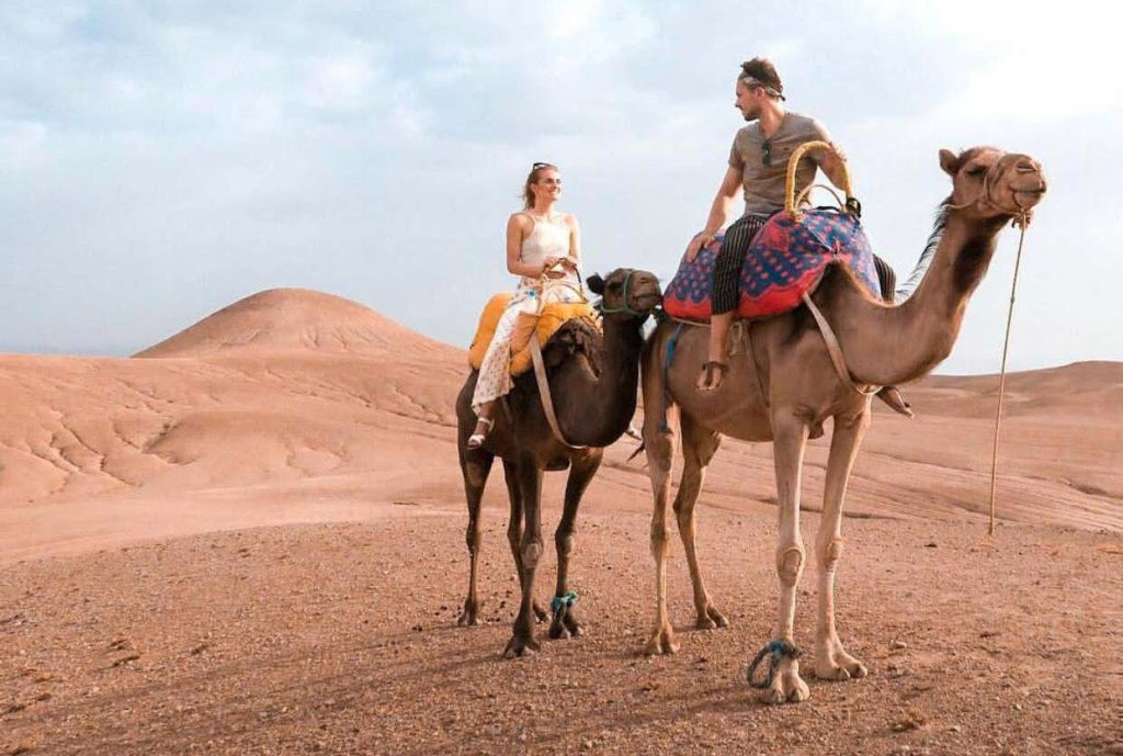 Couple riding camels together in the scenic Agafay Desert with expansive natural landscapes in the background.