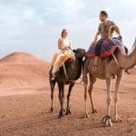 Couple riding camels together in the scenic Agafay Desert with expansive natural landscapes in the background.