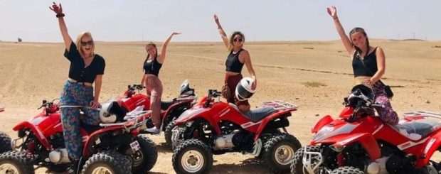 A group of people riding quad bikes in the Agafay Desert, with sand dunes and rocky terrain in the background
